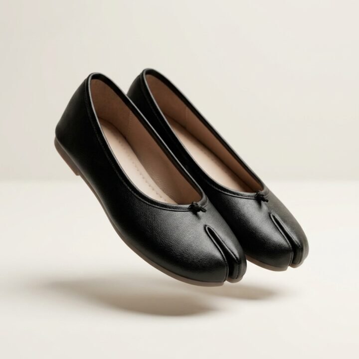 Photo de trois quarts : Vue de trois quarts d’une paire de ballerines tabi femme noires, à bout fendu et petit nœud, sur fond ivoire.